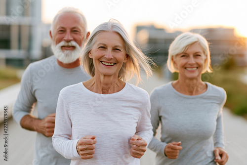 Three smiling seniors jog together at dawn. Their happy expressions show joy and energy. Soft light enhances their peaceful, active moment. Perfect for wellness, retirement, or active lifestyle themes