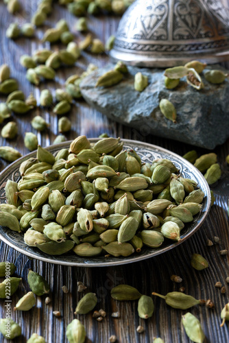 Green cardamom pods in decorative bowl on rustic wooden table
