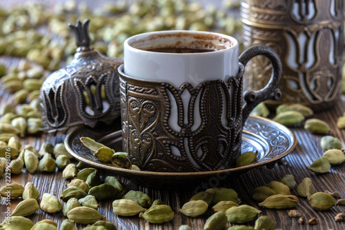 Traditional coffee cup with ornate design surrounded by cardamom pods