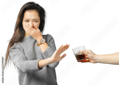 Fotografie Woman covering her mouth and refusing a glass of dark liquid against a white bac