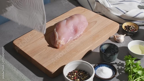Hands pat a raw chicken breast dry with a paper towel on a wooden board beside bowls of seasonings.