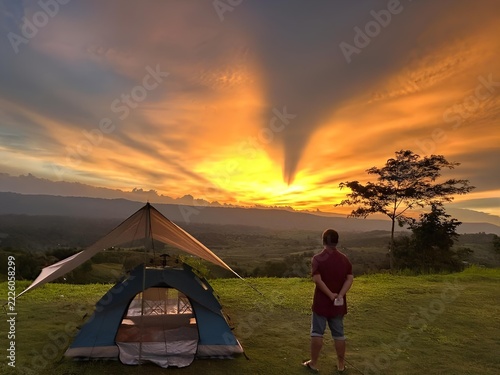 Man camping watching sunset with tent in nature