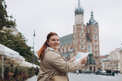 Pretty young woman staying on the street holding paper map in hands. 30s girl in hat posing on Market Square in Krakow. Traveling Europe, High quality photo, Vacation concept