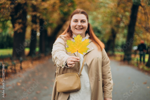 Portrait of pretty young 30s woman in evening autumn park, smiling. Autumn landscape, calmness, tranquility concept. Pretty female holding leaf on nature background. High quality photo.