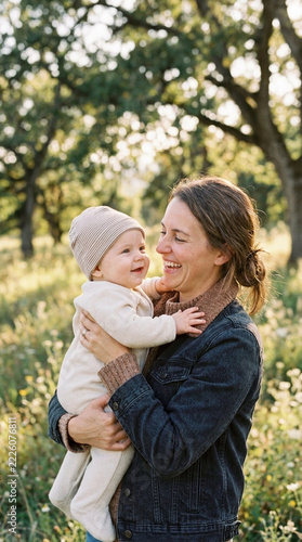 Happy Mother Holding Adorable Baby Outdoors in Sunlight Smiling
