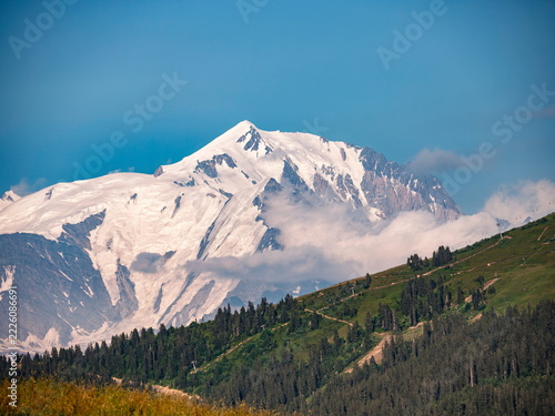 La Giettaz, France - 13.07.2015: Snow-capped Mont Blanc peak towering over lush green alpine forests under a clear blue summer sky