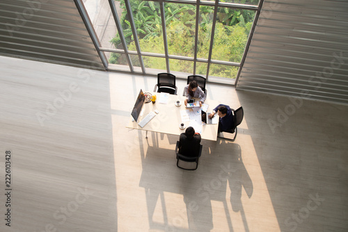 Top view of diverse business people meeting around a table near large glass windows in a modern corporate office, planning financial strategy, teamwork collaboration, and executive brainstorming