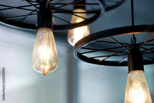 Glowing vintage light bulb with warm golden illumination, Industrial style ceiling pendant lights with black metal wheel frames, glowing bulbs, warm vintage for cafe, restaurant and home interiors