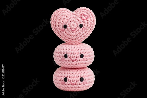 Amigurumi crochet handmade craft of three cute smiling pink characters stacked together with a heart on top, isolated on a black background for a Valentine's Day or love concept.
