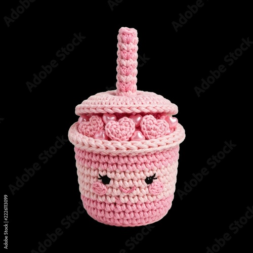 Handmade crochet amigurumi art of a kawaii pink boba tea cup with a smiling face and heart beads, isolated on black for a romantic Valentine's Day gift idea.