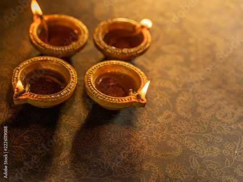 Four Traditional Clay Diwali Diyas with Flickering Flames Arranged on an Ornate Golden Patterned Surface, Warm Festive Close-Up Shot.