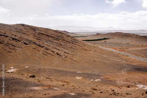 Arid atlas mountains scenery, a long road winding through a barren, dry environment under a cloudy sky