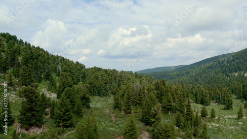 Dense evergreen woodland spreads beneath rounded mountain ridges and a clouded sky near Karakol Lakes, Altai Republic, Russia, showcasing a setting for alpine exploration and tourism