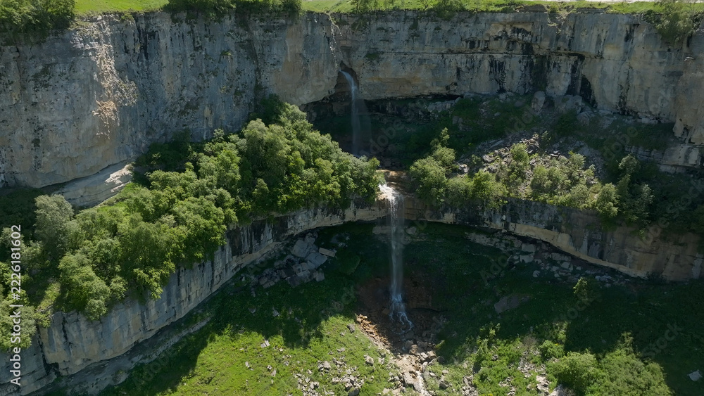 Fototapeta premium Matlas waterfalls descend over pale limestone into a wooded canyon, with layered rock, flowing water and summer greenery forming a scenic highland setting around Matlas in Dagestan, Russia