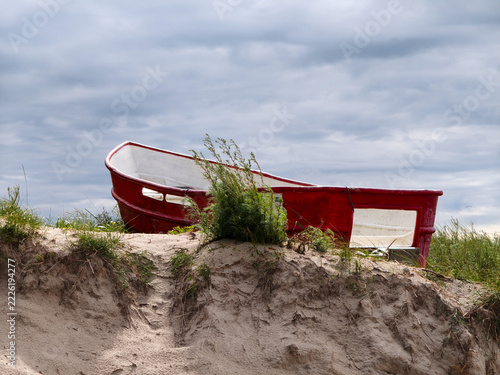 Red Boat On Sand Dune Beach With Overcast Cloudy Sky And Coastal Vegetation