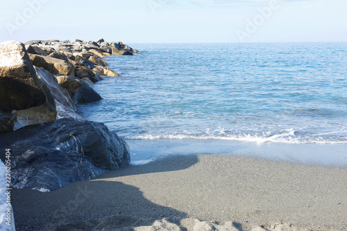 Stone breakwater rocks sea waves Sestri Levante sandy beach coast. Marine geology coastal protection calm blue water horizon. Oceanography natural science earth conservation publishing.