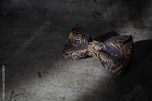 Classic Dark Paisley Luxury Silk Bow Tie on Concrete Background, Captured on a Ray of Light.