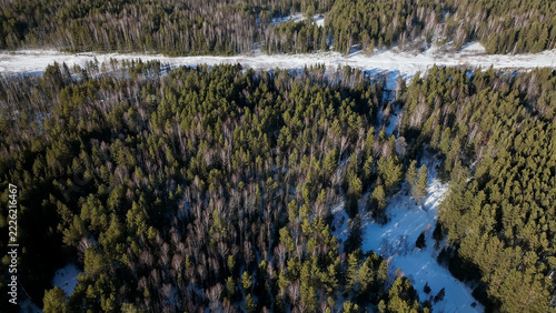 Elevated winter view of a quiet road threading snow-covered pine, spruce, and birch woodland in Russia’s Ural Mountains, with long shadows and a wide, pristine wilderness setting landscape