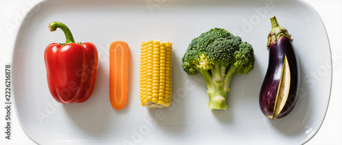 Rainbow Vegetable Flat Lay with Red Bell Pepper, Carrots, Corn, Broccoli and Eggplant Arranged in Color Gradient on White Plate