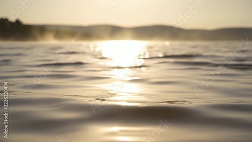 Warm morning sunrise reflecting on calm lake water with gentle ripples and distant misty hills