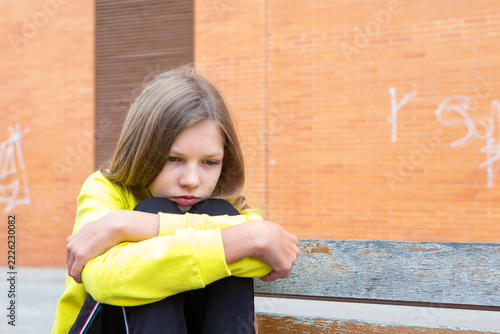 Girl sitting alone on a bench with a sad expression in an urban setting