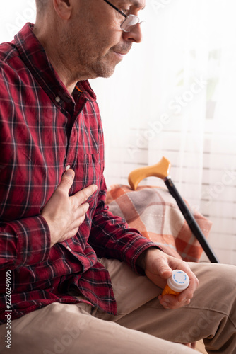 Older Man Experiencing Chest Pain and Holding Medication at Home