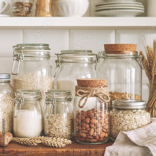 Glass pantry jars filled with dry grains and nuts on a rustic wooden kitchen shelf with copy space