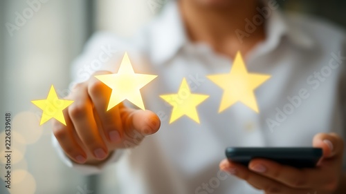 Person holding a smartphone and using their finger to select four glowing yellow stars on a digital interface for customer feedback and rating