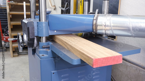 Fotografie Wood thickness planer machine processing a wooden board in a workshop