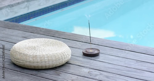 Incense stick releasing smoke on deck, drifting to pool with light breeze blowing, scenting cushion