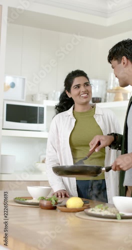 Vertical video: Indian couple plating to serve at kitchen island, man turning food in pan