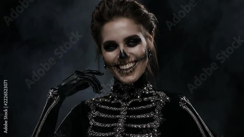 Woman in jeweled skeleton costume smiles and poses with skull face paint. Halloween fashion and costume makeup. Skeleton disguise for seasonal celebration. Gothic style and spooky party