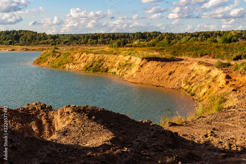 Fotografie Steep sandy quarry slopes descending into a vibrant turquoise lake under a brigh