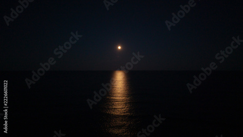 Obraz na plátně Aerial view of full moon over dark ocean at night, golden moonlight reflection on calm sea water surface