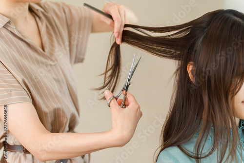 美容室でお客様のロングヘアをハサミでカットする女性美容師。ヘアサロンでの施術風景