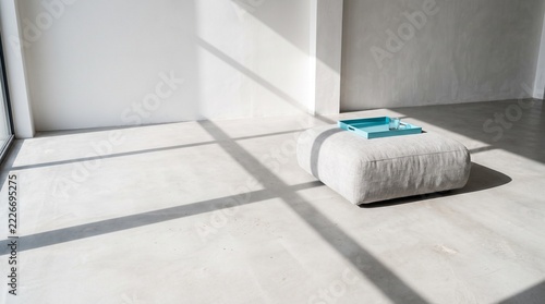 Minimalist sitting space featuring plush ottoman and cyan serving tray casting sharp shadows