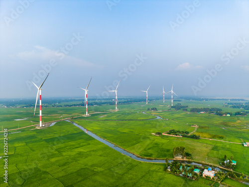 Fotografie High Angle Drone View of Wind Turbines Lineup Over Vibrant Green Paddy Fields in Khurushkul, Cox's Bazar