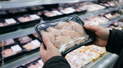 Fresh raw chicken meat in a black plastic tray, hands holding packaged poultry in a supermarket aisle. Uncooked chicken breasts and wings for sale, healthy protein food shopping experience.
