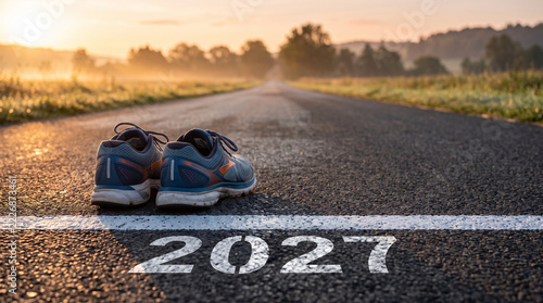 Pair of blue running shoes on asphalt road with 2027 text at early morning