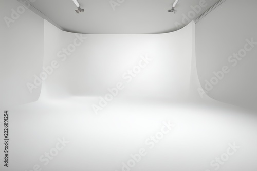 Empty white cyclorama studio with seamless curved backdrop evenly lit by soft diffused overhead lights and minimal shadows leading into smooth floor space for portrait or product photography.
