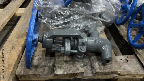 Gray industrial angle valve with blue handwheel and threaded outlet on a wooden pallet, manual flow control, pipeline equipment, warehouse storage
