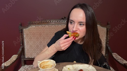 Young woman in black top sitting in vintage chair eating pastry with jam, coffee cup on table, dark red background, cafe interior, eating snack, dessert, coffee break