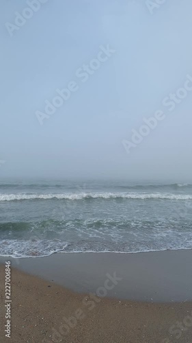 Empty beach in sea fog, calm waves and foam reaching the shoreline, shot vertically in slow-motion
