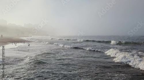 Sea waves wash on sand beach in misty light, with gray horizon in fog