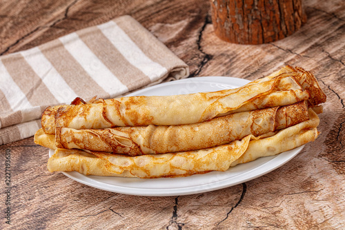 Stack of rolled golden crepes on white ceramic plate with striped linen napkin on rustic wooden table surface breakfast food