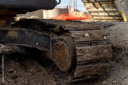 Obraz na plátně Close-up of a mud-covered steel crawler track and undercarriage of an excavator on rough soil at a construction site; track plates and part of the machine are visible