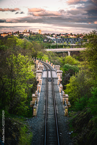 Old stone railway viaduct stretching over a lush green valley toward distant city buildings at twilight