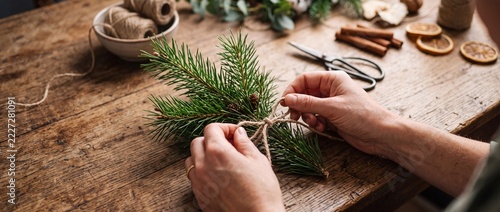 Making Handmade Christmas Decoration with Pine Branch and Twine on Wooden Table
