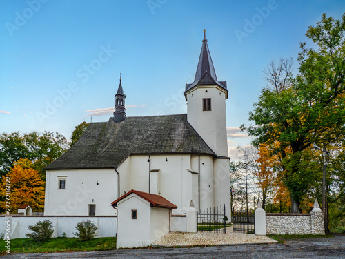 Historic White Church With Steeple and Walled Courtyard Surrounded by Autumn Trees at Dusk