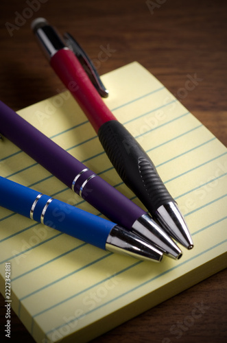 Purple, Blue and Red Fountain Pens with Yellow Notepad on Wood Table Vertical